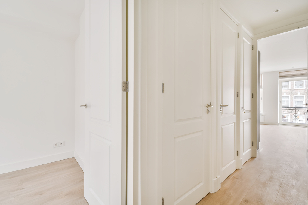 A perspective view of an empty narrow hallway with white walls and parquet floors in a minimalist apartment.